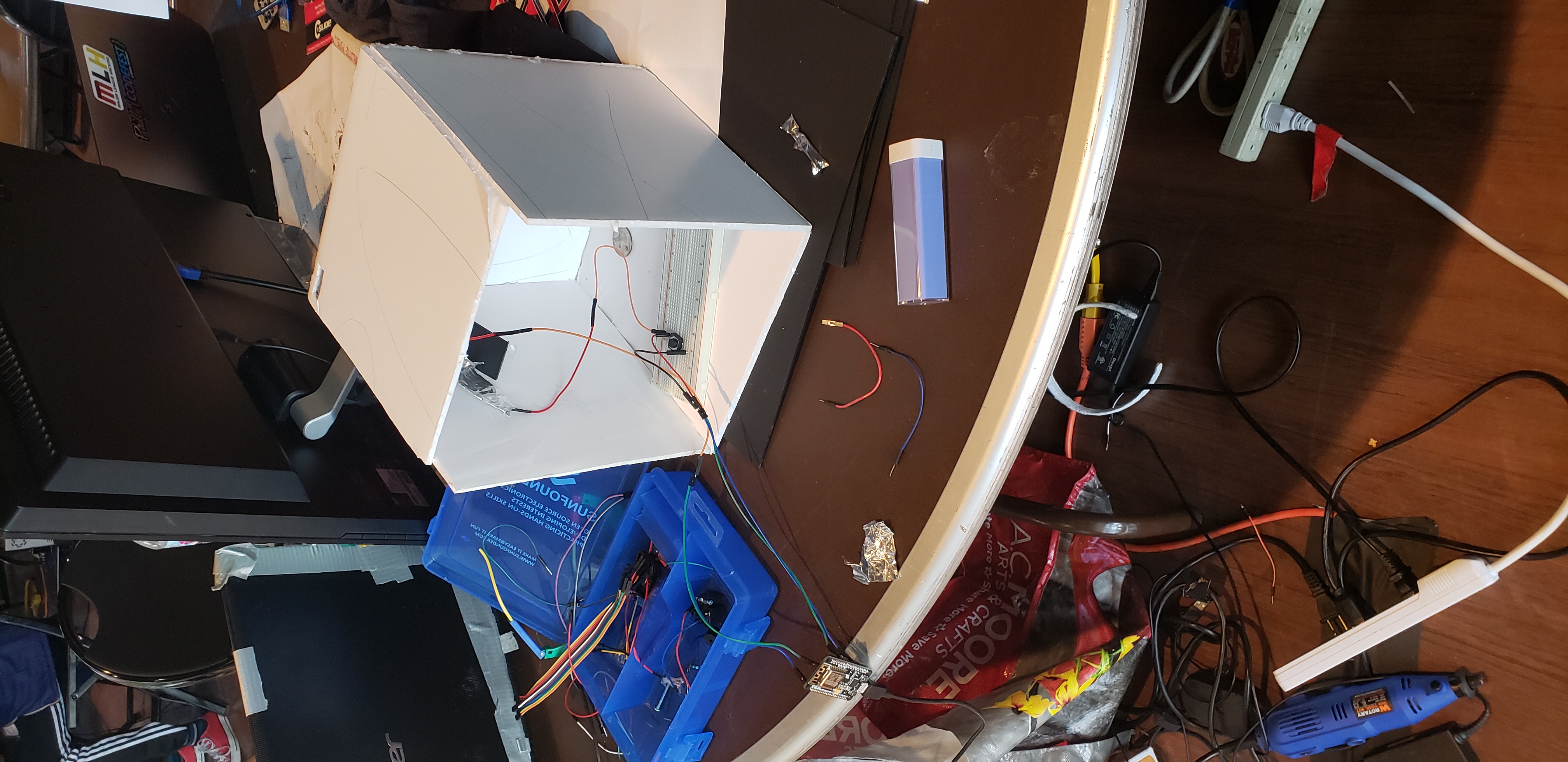 PennyBin’s early white enclosure with a breadboard, wiring, and electronics on a worktable.