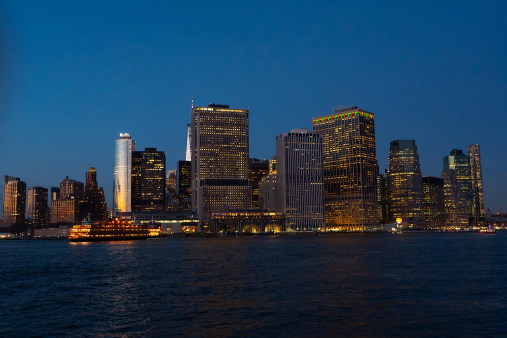 An illuminated waterfront skyline and ferry at blue hour.
