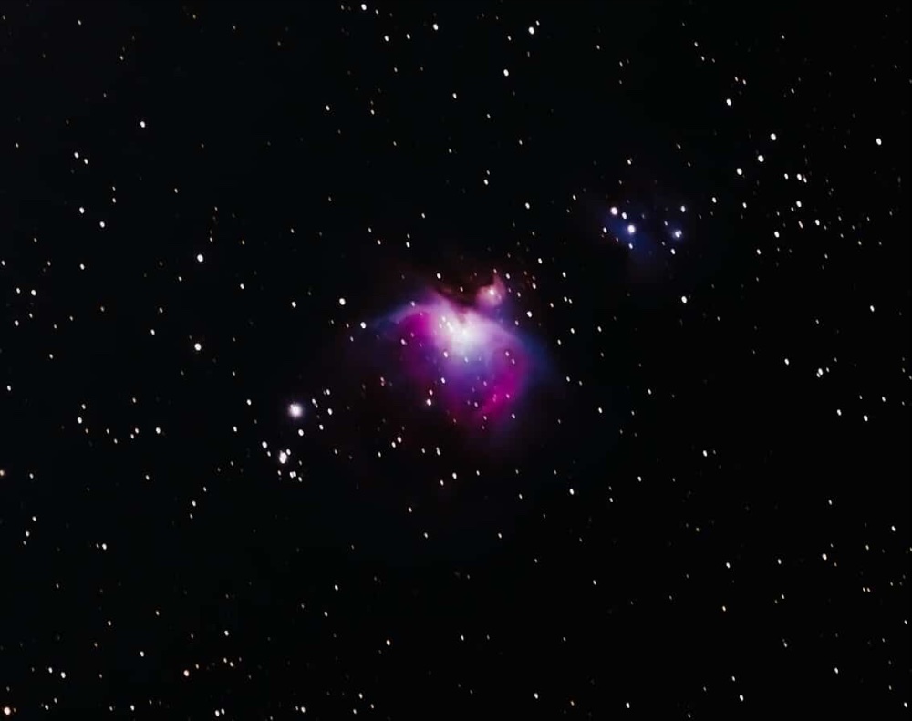 The Orion Nebula glowing pink and violet, surrounded by stars against a dark sky.